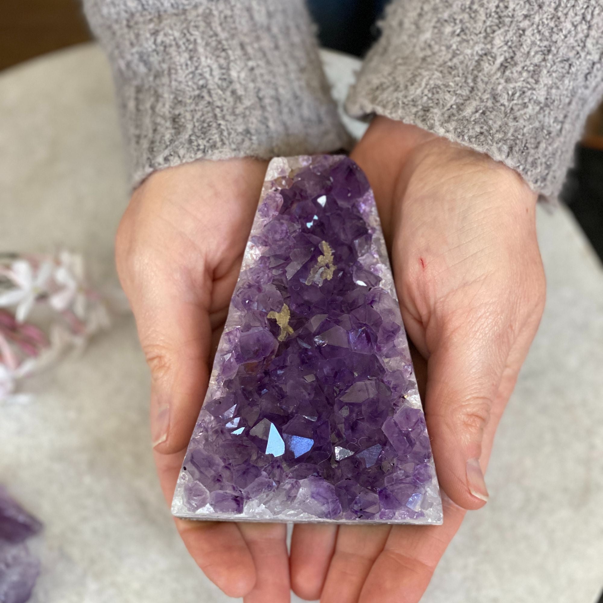 Hands hold a large, flat, deep purple amethyst crystal cluster, 4 inches tall.