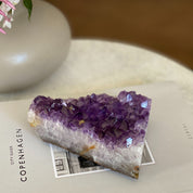 Large, flat deep purple amethyst crystal cluster with sparkling facets on a book.