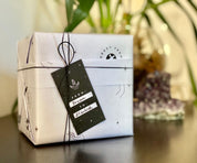 White celestial gift wrap with black twine and a personalized "FROM: Bryan TO: Elizabeth" tag. Amethyst crystal set in background.
